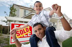 Hispanic Father and Son in Front of Their New Home with Sold Home For Sale Real Estate Sign.